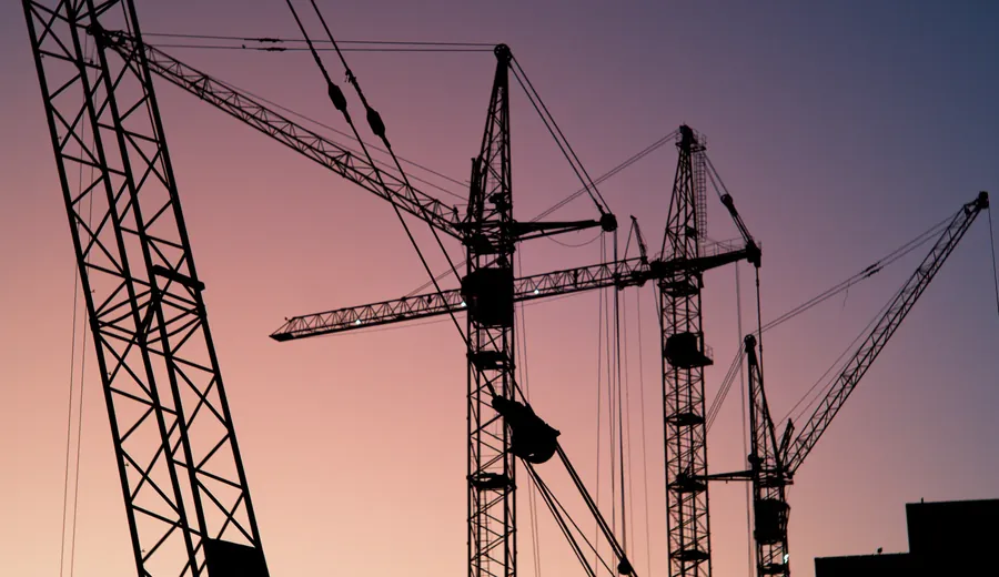 Tower cranes silhouetted against a dusk sky