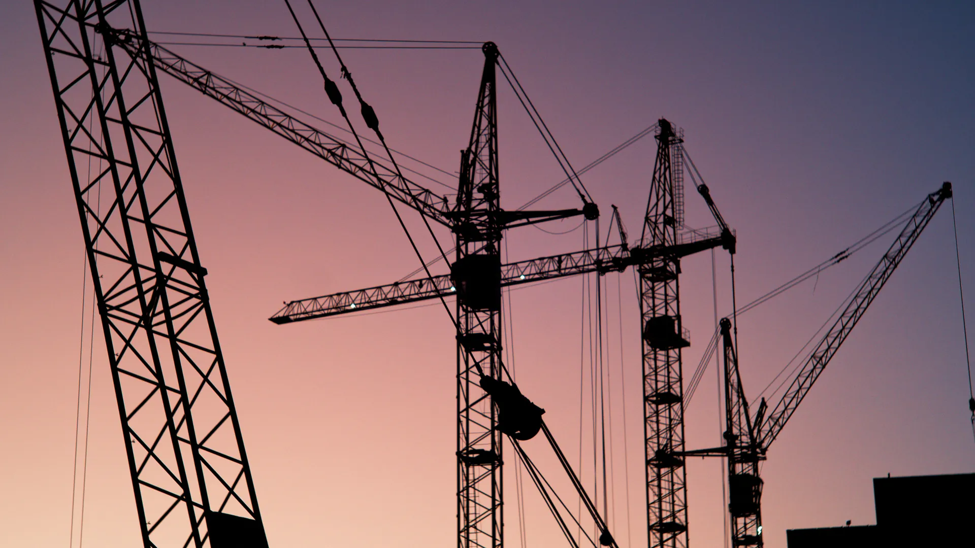 Tower cranes silhouetted against a dusk sky over a construction site